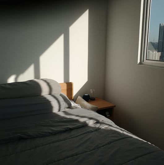 Nowoczesna sypialnia z łóżkiem i oknem, przez które wpada światło słoneczne.