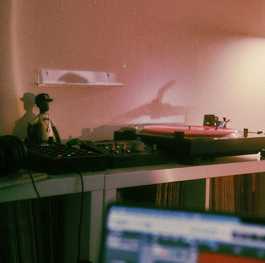 Gramofon i sprzęt DJ-ski ustawione na białym regale, z rozmytym laptopem na pierwszym planie.